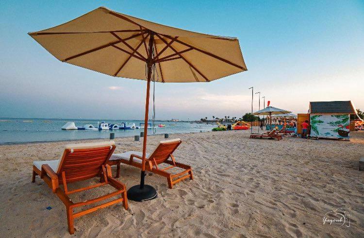 zwei Stühle und ein Sonnenschirm am Strand in der Unterkunft فيلاً بالقرب من البحر in Al Fanātīr