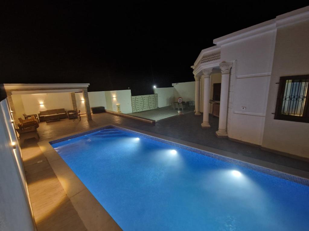 a large swimming pool in the middle of a house at night at Belle villa Zarzis in Zarzis
