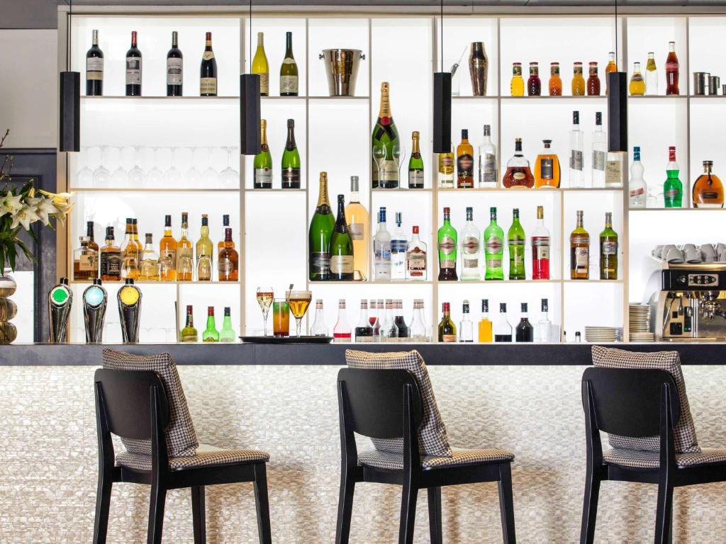 a bar with three chairs and bottles of alcohol at Mercure Caen Cote De Nacre in Caen