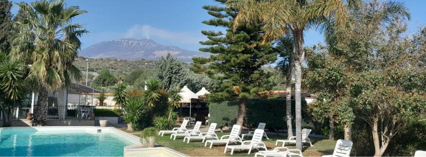 a pool with white lounge chairs and a mountain at Agrihotel Croce Vallone in Biancavilla