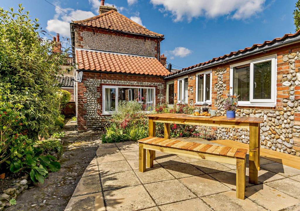 a wooden bench in front of a brick house at Hidden Loke Cottage in Blakeney