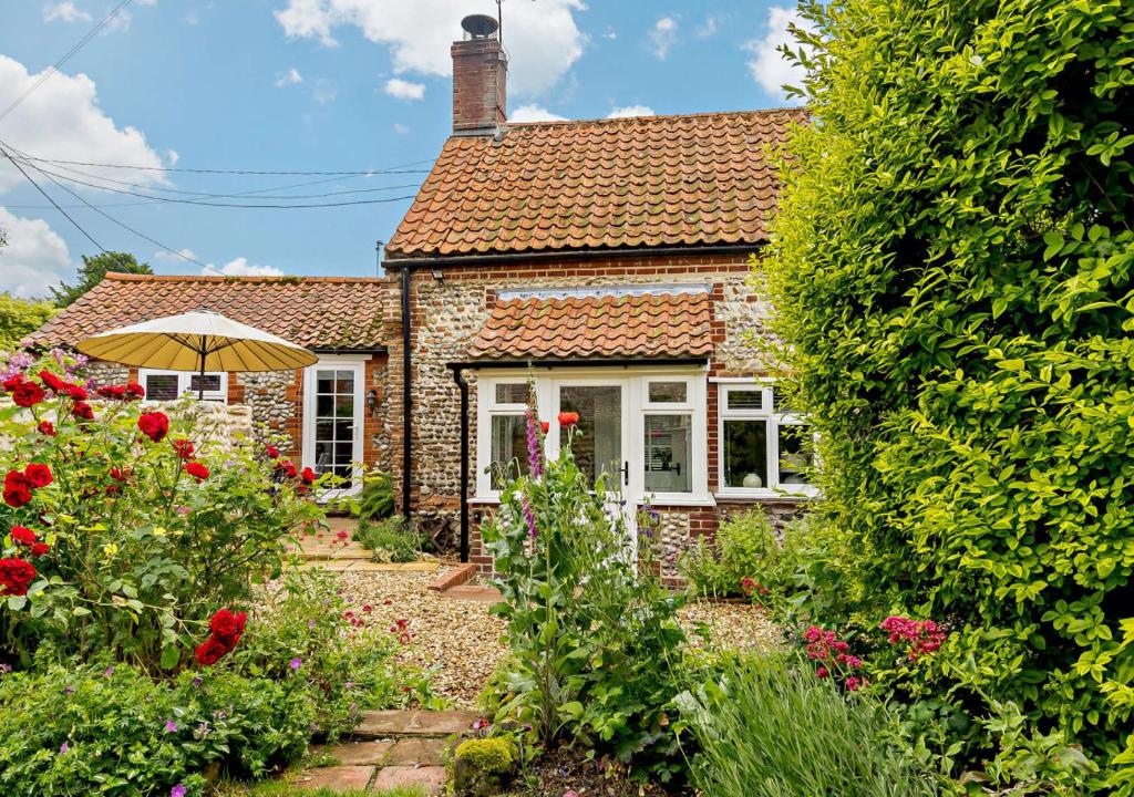 a brick cottage with an umbrella in the garden at Dolphin Cottage in Wiveton