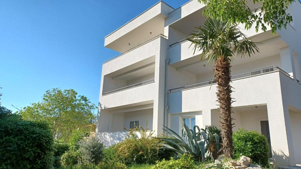 a white building with a palm tree in front of it at Apartments Daria in Krk