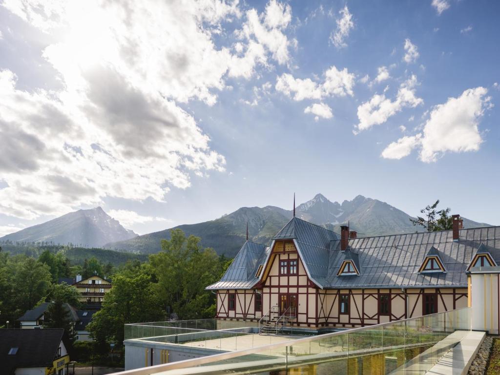 a building with a roof with mountains in the background at Hotel Lomnica in Vysoke Tatry - Tatranska Lomnica.