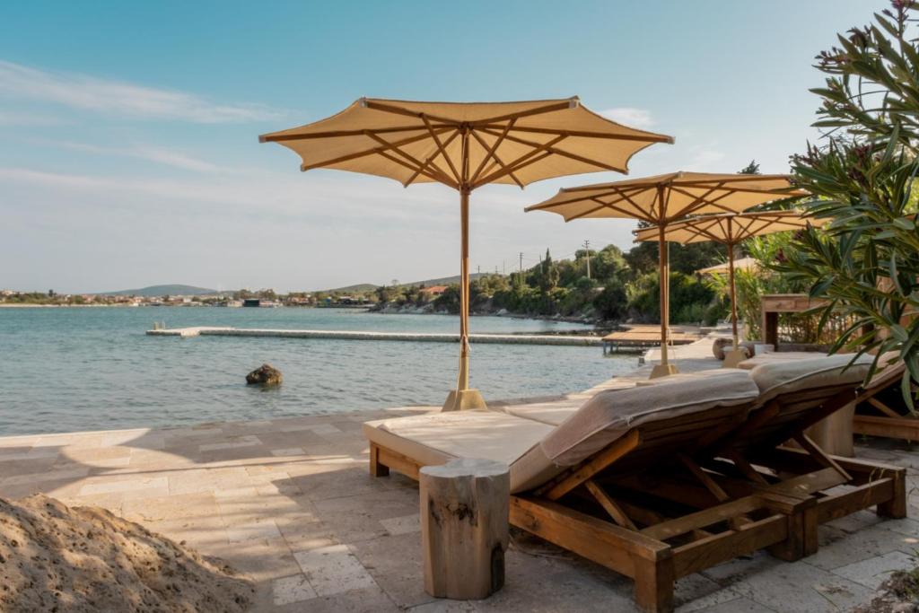 a beach with benches and umbrellas and the water at GAIA Alaçatı BY THE SEA - Adult Only in Çeşme