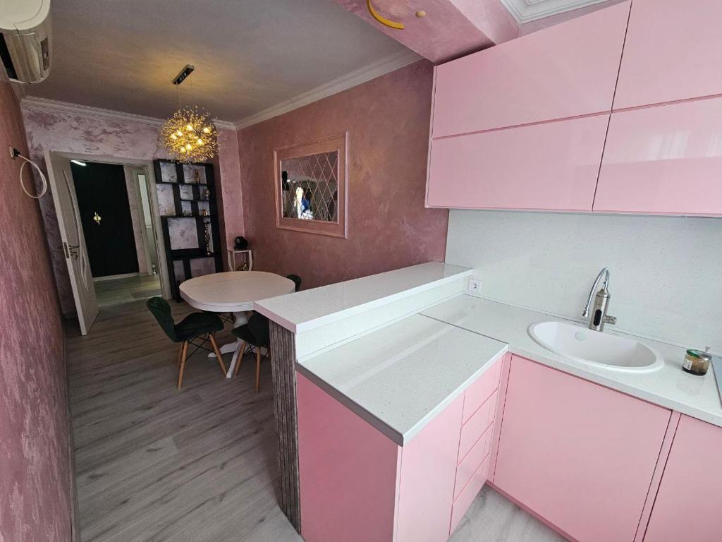 a pink kitchen with a sink and a table at Апартамент Елинор in Pomorie