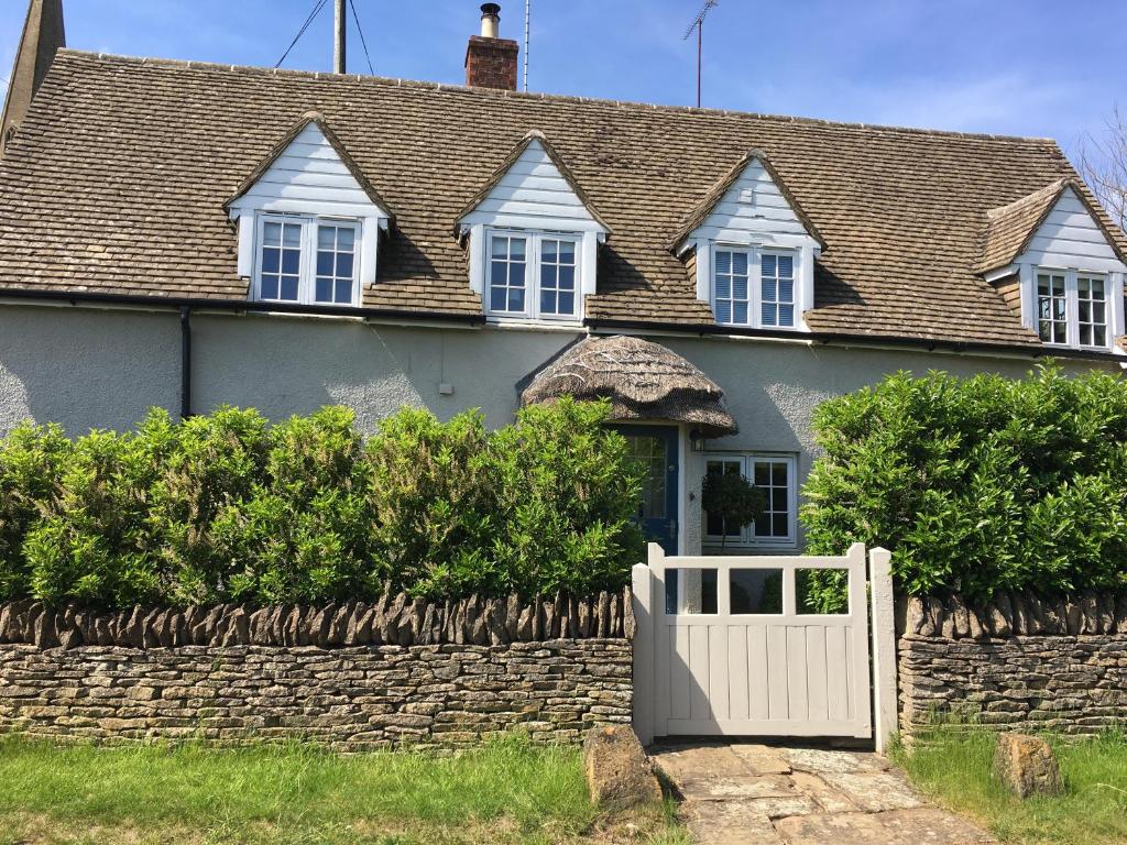 een huis met een witte poort en een stenen hek bij Thatch Cottage in Todenham