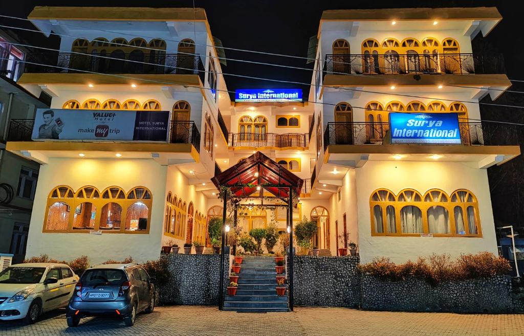 un bâtiment avec des voitures garées devant lui dans l'établissement Hotel Surya International - Manali, à Manali