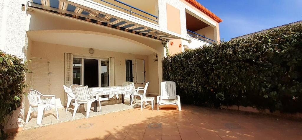 un patio avec des chaises blanches et une table et une haie dans l'établissement OREE DU GOLF II Joli T3 proche golf piscine Cap d Agde, au Cap d'Agde