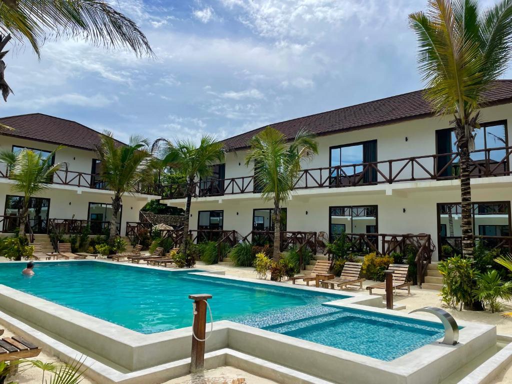 a pool in front of a hotel with palm trees at Sand Beach Boutique Hotel in Bwejuu