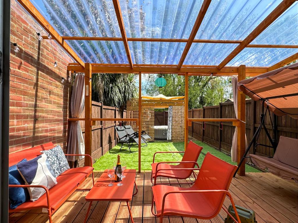 a pergola with red chairs and a table on a deck at Luxury 2-bedroom Townhouse in Central Canterbury with Hot Tub, Garden & Private Parking! in Canterbury