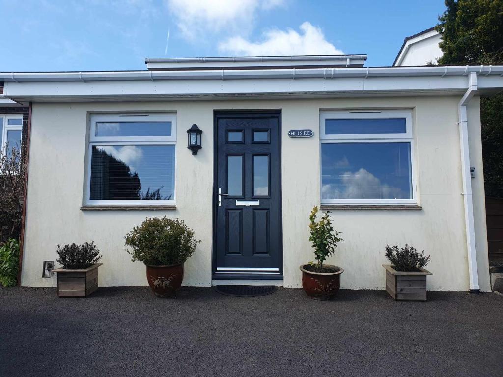 a white house with a black door and two potted plants at Hillside in St Austell