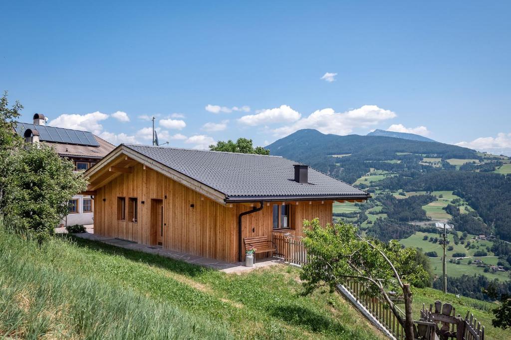 une maison en bois sur une colline avec des montagnes en arrière-plan dans l'établissement HAUSERHOF - Urlaub auf dem Bauernhof in Villanders mit einzigartigem Ausblick in die Dolomiten, à Villandro