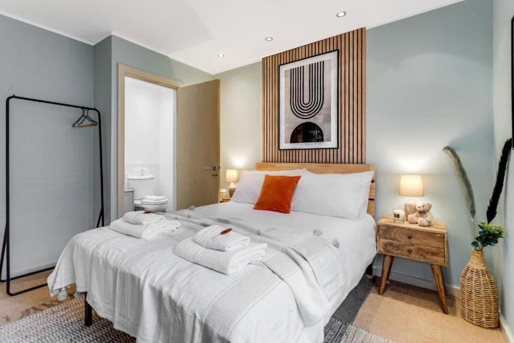 una camera da letto con un grande letto con lenzuola bianche e cuscini arancioni di City Stays Hideaway Luxury Townhouse in Canterbury, sleeps 6 a Canterbury
