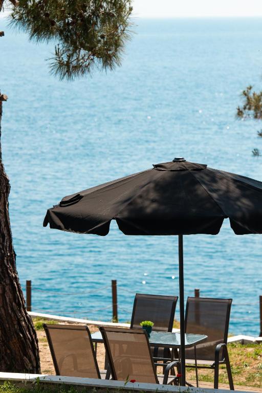 a table and chairs under an umbrella near the water at Acroterra - Easy Living in Alyki