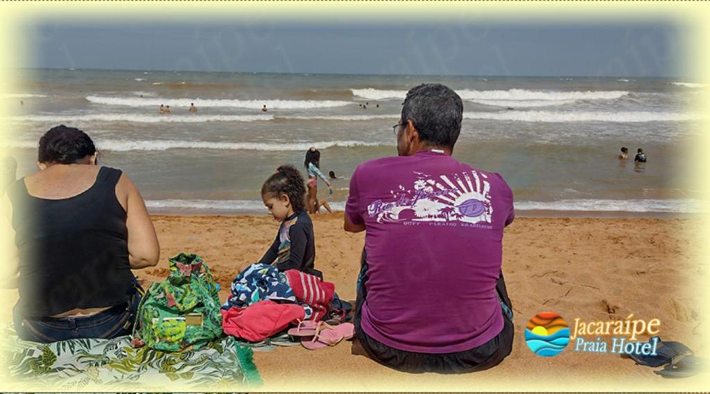 grupa ludzi siedzących na plaży patrzących na ocean w obiekcie Jacaraipe Praia Hotel w mieście Serra