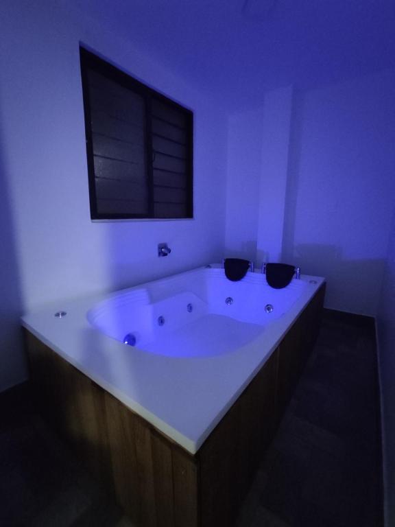 La salle de bains blanche est pourvue d'une grande baignoire et d'une fenêtre. dans l'établissement Apartamento con jacuzzi En Bello - Cerca a Medellín, à Bello