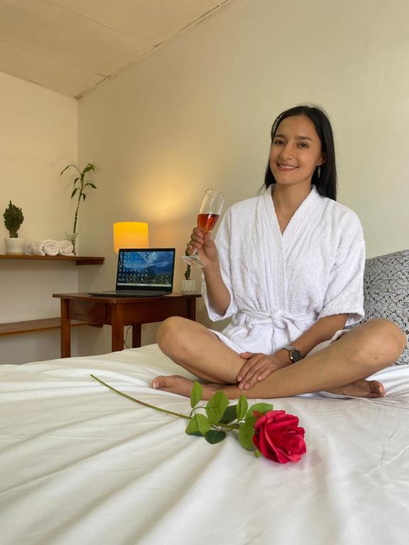 eine Frau, die auf einem Bett sitzt und ein Glas Wein hält in der Unterkunft Irigoin Hospedaje in Nueva Cajamarca