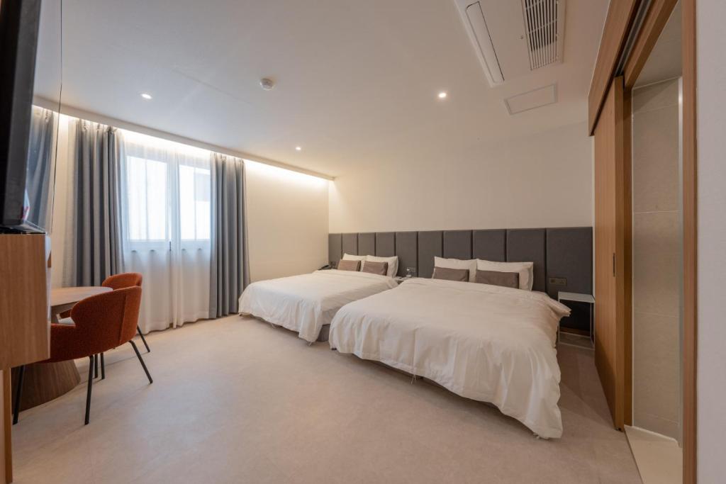 a hotel room with two beds and a table and a desk at H-avenue Hotel Munhyeon in Busan