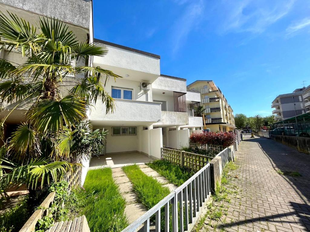 a white building with a palm tree next to a sidewalk at Refreshing villa with private garden near the beach in Porto Santa Margherita di Caorle