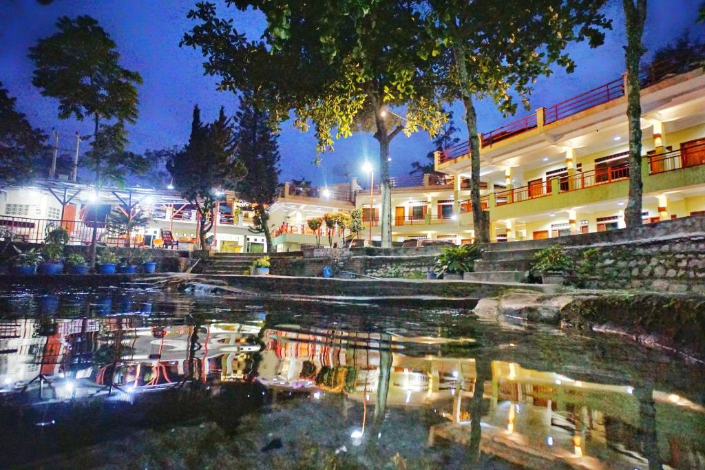 a building with a reflection in the water at night at Pandu Lakeside Hotel Parapat in Parapat