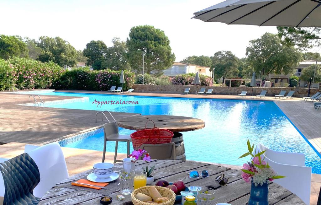 a table with food and an umbrella next to a swimming pool at Appart Cala Rossa - T2 Porto-Vecchio in Lecci