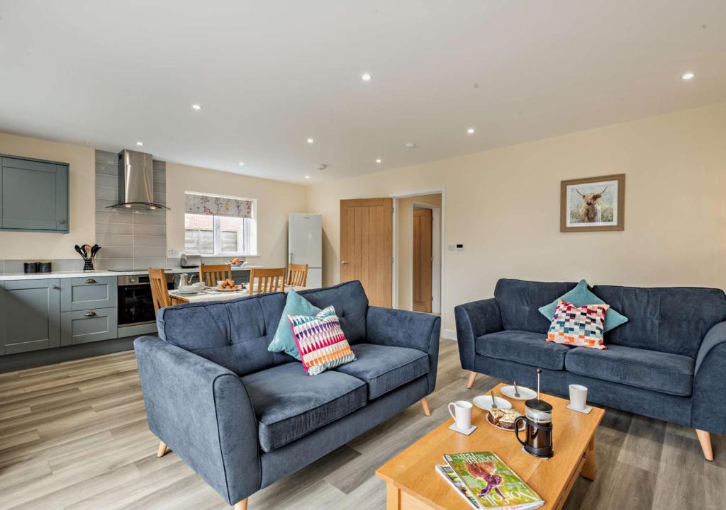 a living room with two blue couches and a kitchen at Sea Glass - Sheringham in Sheringham