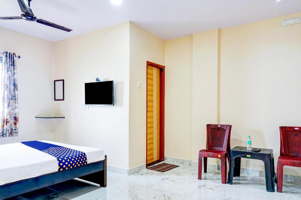 een slaapkamer met een bed en twee stoelen en een televisie bij SPOT ON Hotel Shree Samarth Lodging in Kolhapur