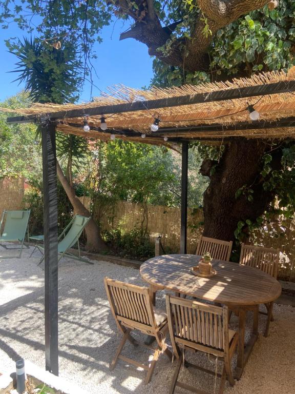 een houten tafel en stoelen onder een pergola bij Rez de villa avec jardinet proche de la plage in Hyères