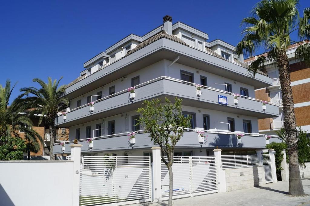 a white building with a white fence and palm trees at Palazzina Cala Luna Suite in San Benedetto del Tronto