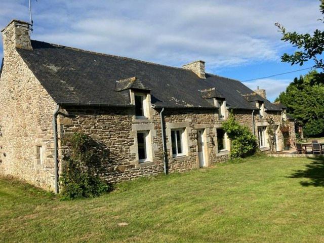 une ancienne maison en pierre avec une pelouse devant elle dans l'établissement Longère familiale - SAINT POTAN, à Saint-Potan