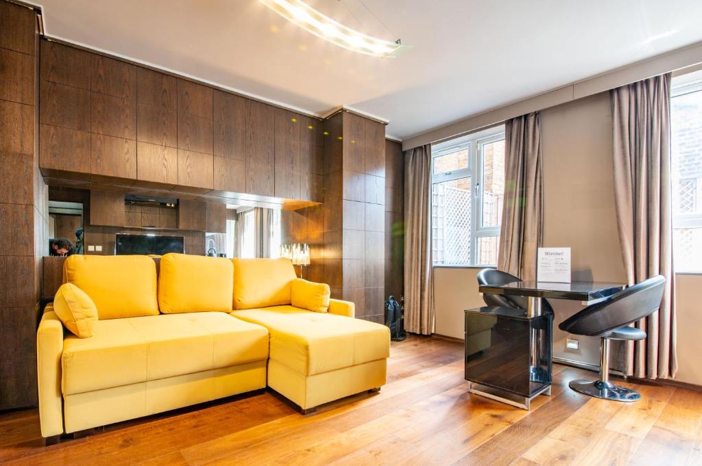 a yellow couch in a living room with a desk at Luxury Studio Flat Victoria SW1 in London