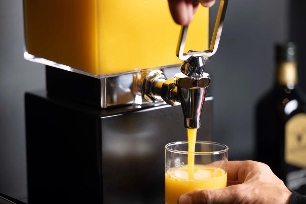 a person pouring an orange juice into a glass at Hotel D - Strasbourg in Strasbourg