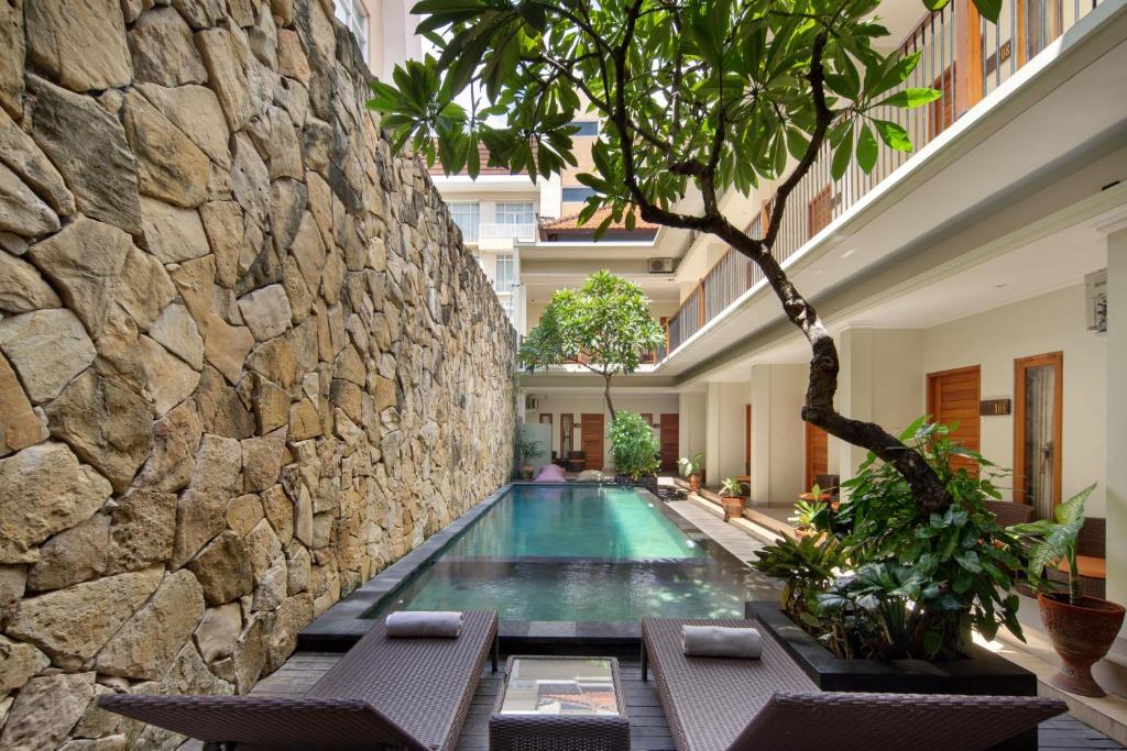 una piscina en un edificio con una pared de piedra en Angkul Angkul Segara Beach Kuta by Kamara en Kuta