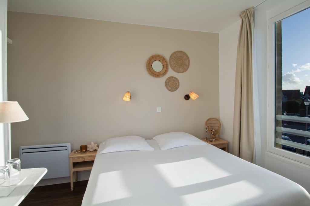 - une chambre blanche avec un grand lit et une fenêtre dans l&#39;établissement Hôtel De La Plage, à Courseulles-sur-Mer