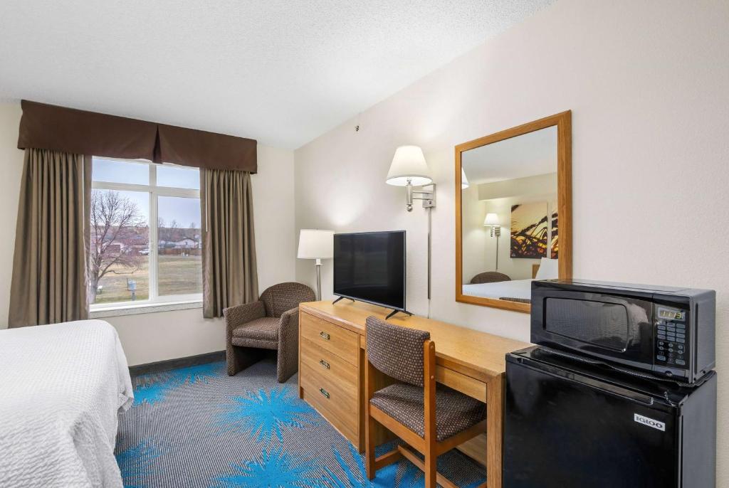 a hotel room with a desk and a bed and a television at Days Inn by Wyndham Great Falls in Great Falls