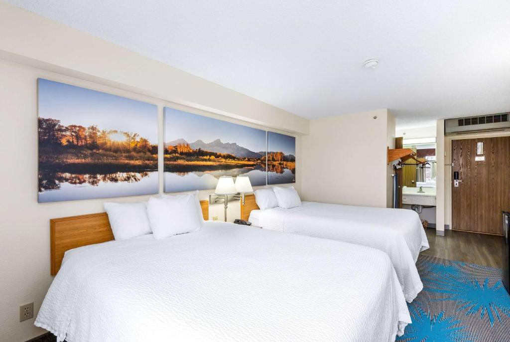 two beds in a hotel room with a painting on the wall at Days Inn by Wyndham Great Falls in Great Falls