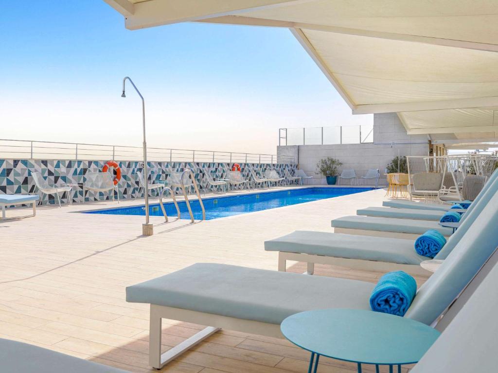 une piscine avec des chaises longues bleues et une piscine dans l'établissement Novotel Sevilla, à Séville