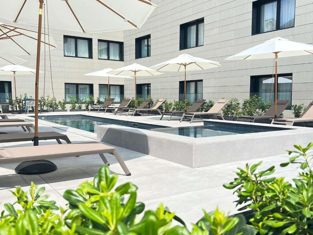a pool with chairs and umbrellas next to a building at Novotel Parma Centro in Parma
