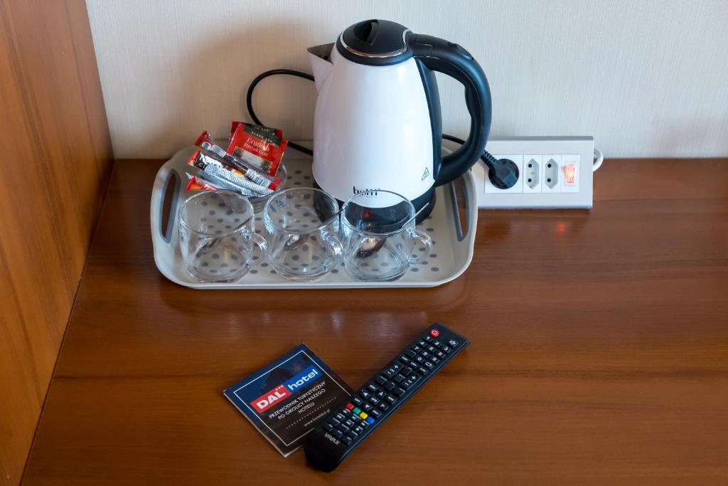 Electric kettle with cups on tray and TV remote on wooden desk, guest refreshment setup