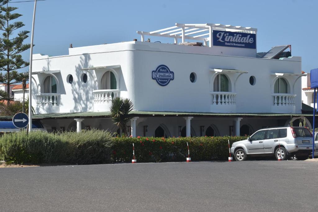 un edificio blanco con un coche aparcado delante de él en Hotel L'Initiale, en Oualidia