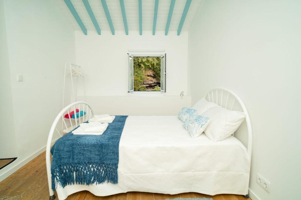 una camera da letto bianca con un letto bianco e una coperta blu di H2O - próximo das melhores praias da costa sul a Vila Franca do Campo
