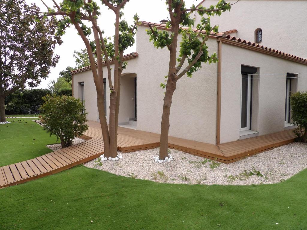 un jardin avec deux arbres et une terrasse en bois dans l'établissement St Cyprien Charmante maison proche du port et des plages, à Saint-Cyprien