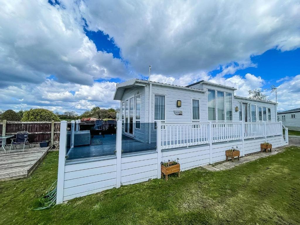 a white house with a deck and a yard at Beautiful 6 Berth Caravan With Decking At Dovercourt Park, Essex Ref 44009g in Great Oakley