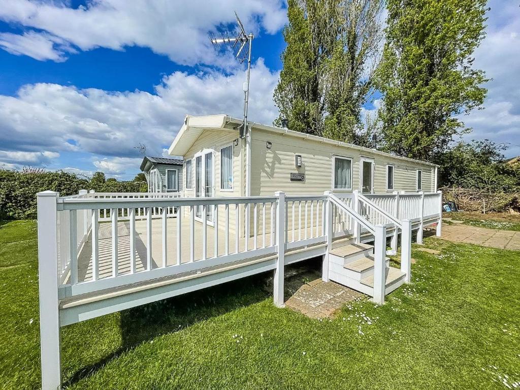 a small white house with a white fence at Gorgeous 6 Berth Caravan With Decking Area, Dovercourt Holiday Park Ref 44010af in Great Oakley