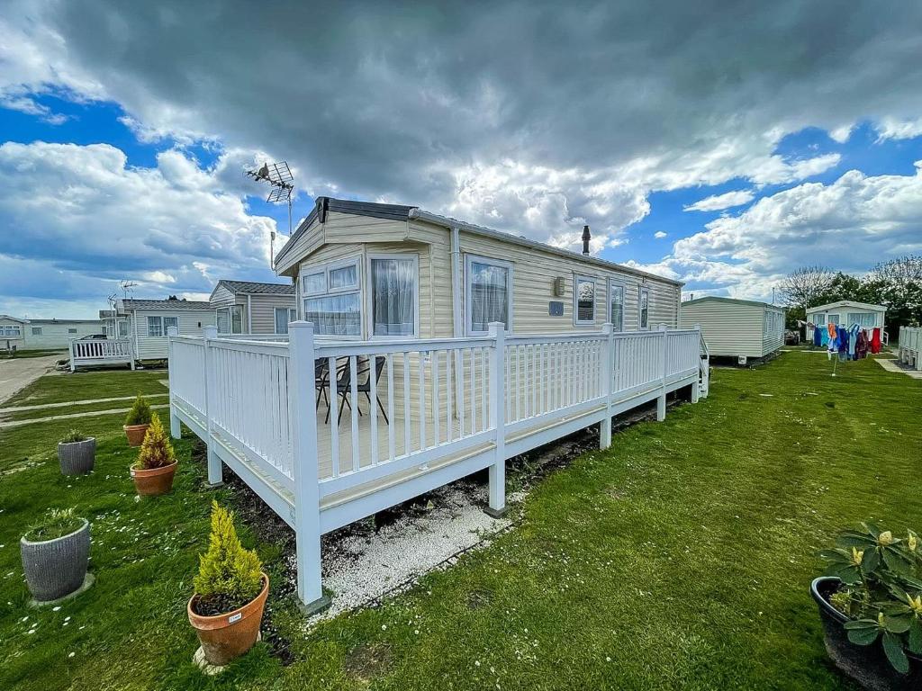 a white house with a white fence in a yard at Gorgeous 6 Berth Caravan With Large Decking Area, Essex Ref 44009f in Great Oakley