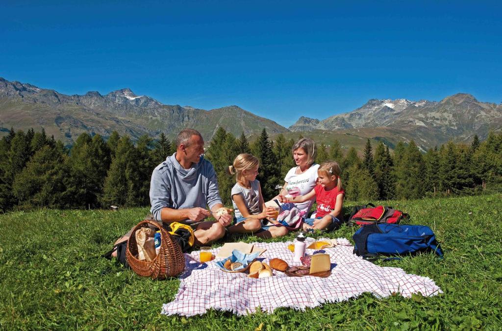 una familia sentada en una manta de picnic en la hierba en Hotel Arlecchino - Dada Hotels en Madesimo