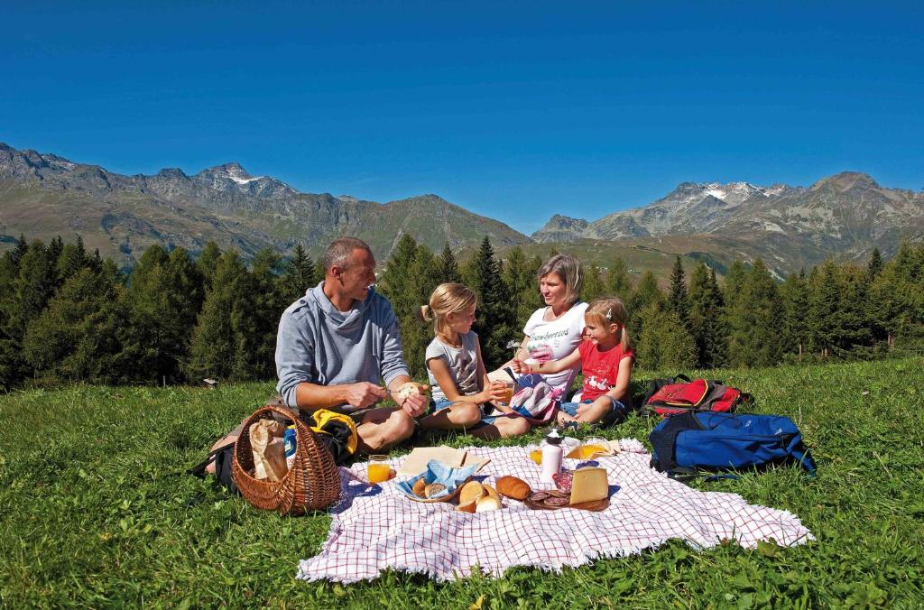 a family sitting on a picnic blanket in the grass at Hotel Arlecchino - Dada Hotels in Madesimo