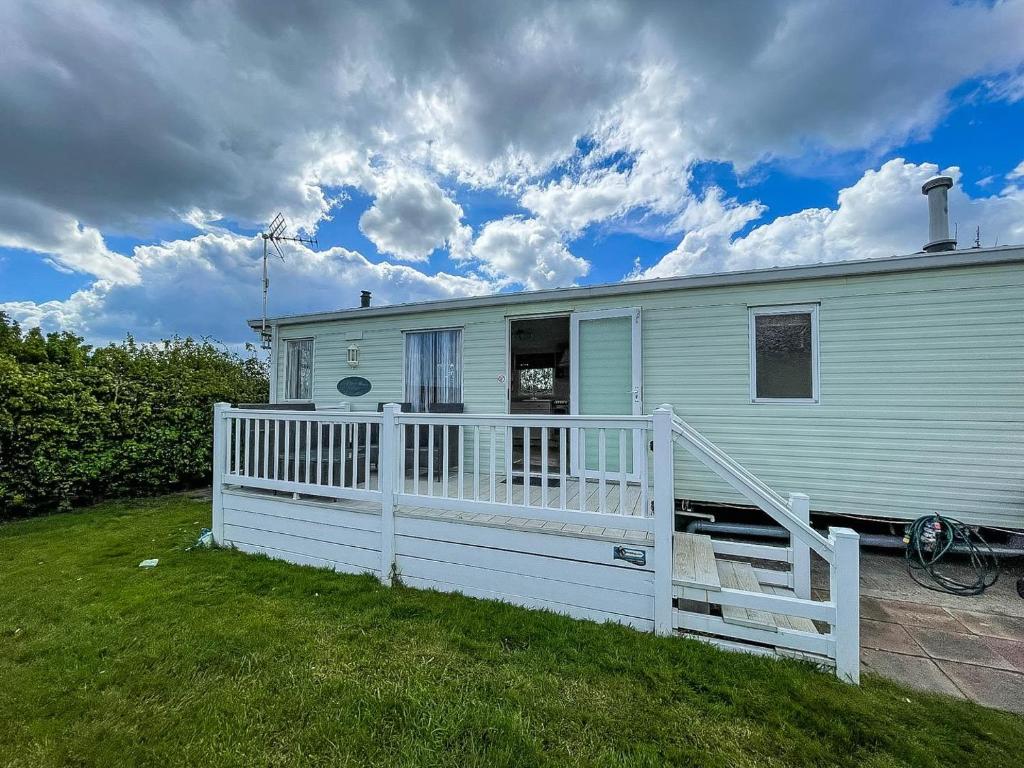 uma casa branca com um alpendre e uma cerca branca em Brilliant Caravan With Decking And Wifi At Dovercourt Park In Essex Ref 44010a em Great Oakley