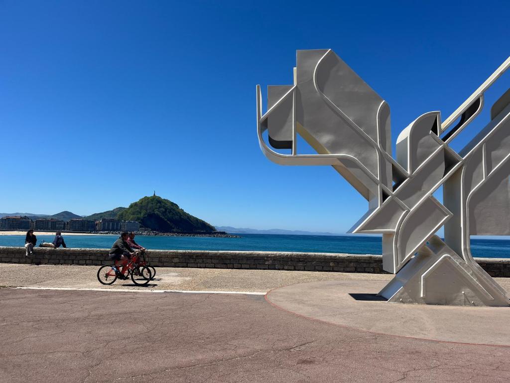 una persona montando una bicicleta junto a una escultura de metal en Sagues Beach Apartment, en San Sebastián